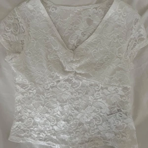 Vit spetsblus med v-ringning - Superfin vit blus i spets med blommigt mönster och v-ringad hals. Storlek 10 y men skulle säga att det passar xxxs/xxs om man vill ha den kort! 