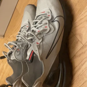 Nike React Element 55 sneakers grå - Nike React Element 55 sneakers i ljusgrått med svarta detaljer och röda accenter. Snygg design med synlig snörning och stor svart Swoosh på sidan. Ovandel i syntetmaterial och mesh för bra andningsförmåga. Mjuk och responsiv React-sula för extra komfort. Kan rengöra innan jag skickar