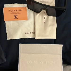 Svarta solglasögon  - Säljer ett par svarta solglasögon med breda, matta bågar och rektangulär form. Glasen är mörka och bågarna har diskret logga på sidan. Kommer med originalfodral, putsduk och certifikat. Riktigt snygga och exklusiva.