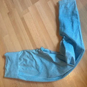 Ljusblå träningstights från Complete - Snygga ljusblå träningstights från Complete med diskret prickigt mönster längs benen och logga på höften. Tightsen har bred mudd i midjan och är gjorda i ett stretchigt syntetmaterial som sitter tight och bekvämt under träningen.