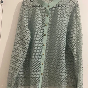 Mintgrön spetsblus med knappar - Superfin mintgrön blus i spets med genomgående knappar framtill. Blusen har lång ärm och ett unikt blommigt spetsmönster som ger en luftig och cool känsla. Perfekt för dig som vill sticka ut med en romantisk och trendig look.