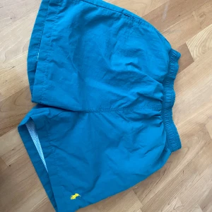  badshorts från Polo Ralph Lauren - Nya aldrig använda. Snygga badshorts från Polo Ralph Lauren med gul broderad logga framtill. Färgen är grön blå. Shortsen har elastisk midja och innerbyxa i mesh. Perfekta för stranden eller poolen. Står storlek medium men de är som small. Därför listar jag dem som small. Nypris 500 kr 
