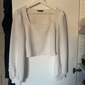 Vit croppad topp med puffärm från SHEIN - Superfin vit croppad topp från SHEIN med fyrkantig ringning och långa puffärmar. Tjockare struktur i tyget och breda muddar vid ärmsluten ger en snygg siluett. Perfekt att styla med höga jeans eller kjol.