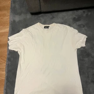 Vit t-shirt MAN med blå OFCL-tryck - Vit t-shirt från MAN med stor, blå OFCL-text på ryggen i en cool, vågig font. Klassisk rund hals och korta ärmar. Mjuk och skön bomullskvalitet, perfekt för dig som gillar streetwear och grafiska prints.