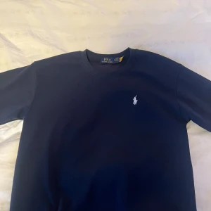 Mörkblå sweatshirt från Polo Ralph Lauren - Klassisk mörkblå sweatshirt från Polo Ralph Lauren med rund halsringning och broderad vit logga på bröstet. Tröjan har ribbade muddar vid ärmslut och nederkant. Perfekt för en clean och stilren look. Tröjan är använd en gång bara. Nypris 899kr, storlek S. Priset kan diskuteras vid snabb affär.