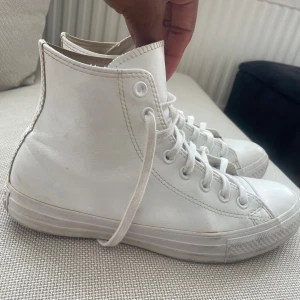 Vita Converse All Star i skinn - Säljer ett par klassiska vita Converse All Star high-tops i skinn. Skorna har rund tå, snörning och den ikoniska loggan på sidan. Perfekta för dig som gillar en clean och stilren look med streetkänsla.