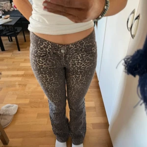 Leopardmönstrade bootcut jeans - Säljer ett par snygga jeans med leopardmönster i bruna och beige toner. Byxorna har låg midja och bootcut-snitt som ger en cool siluett. Perfekta för dig som vill sticka ut lite extra.