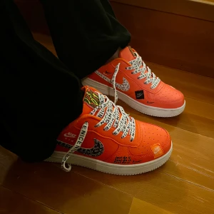 2018 Nike Air Force 1 Premium Just Do It orange (Limited Edition)  - Limited Edition Nike Air Force 1 sneakers i orange med vit sula och svarta detaljer. Swoosh-loggan har textprint och skorna har breda vita skosnören med svart text. Perforerad tå och klassisk Air-dämpning. Perfekta för dig som vill sticka ut eller är en samlare. Äkta skinn. (Unisex)
