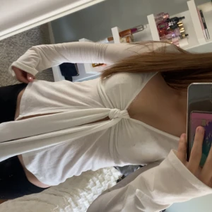 Vit omlottopp med knyt framtill - Trendig vit omlottopp med lång ärm och djup v-ringning. Toppen har en snygg knytning framtill som ger en cool och modern look. Perfekt att styla med jeans eller kjol för en fräsch outfit.