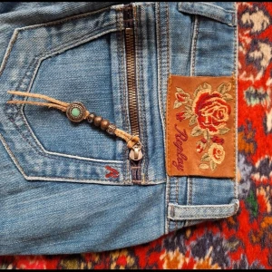 Replay jeans med broderad patch & detaljer - Unika ljusblå jeans från Replay med broderad ros-patch på bakfickan, dragkedjor och dekorativa band med pärlor och turkosdetaljer. Snyggt paisleymönstrat innerfoder och klassisk femficksmodell. Perfekta för dig som vill sticka ut med coola detaljer. Modell:low W30 L32 innerbenslängd 83 