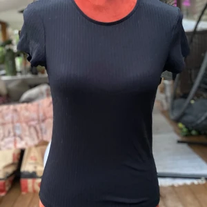 Svart ribbad t-shirt från Bik Bok S - Svart, ribbad t-shirt med rund hals och korta ärmar.  65 % polyester ﻿30% viskos ﻿5 % elastan ﻿Längd: 57 cm ﻿Bystvidd: 43 cm. Katter finns i hemmet! 01