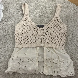 Beige stickad och broderad linnetopp Primark - Supersöt linnetopp från Primark med stickad beige överdel och broderad, vit volang nertill. Toppen har breda axelband, knappar framtill och fina hålmönster både i stickningen och i tyget. Perfekt för en somrig och chill look!