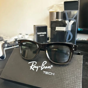 Svarta Ray-Ban Tech Wayfarer - Snygga svarta Ray-Ban Tech Wayfarer-solglasögon med klassisk fyrkantig form och diskreta silvriga detaljer vid bågens front. Glasögonen har Ray-Ban-logga på både lins och skalmar. Perfekta för dig som vill ha en tidlös och cool look.