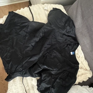 Svart omlottklänning från Old Navy - Svart omlott blus från Old Navy med puffiga korta ärmar och knytband i midjan. Blusen har en v-ringad hals och är tillverkad i ett lätt, vävt material som ger en snygg siluett. Perfekt för dig som gillar stilrena och enkla plagg. Köpt i usa