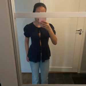 Mörkblå blus med knyt och puffärm - Marinblå blus med tre söta knyt framtill och puffiga korta ärmar. Perfekt att styla med jeans eller kjol.