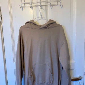 Beige hoodie från New Black - Säljer en stilren beige hoodie från New Black i storlek S. Hoodien har en klassisk känguruficka framtill, huva och ribbade muddar vid ärmslut och nederkant. Perfekt för en chill och avslappnad look.