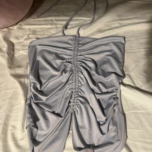 Grå kort topp med snörning - Säljer min tröja från pull&bear den är helt ny jag har aldrig använd den. Supersnygg grå kort topp med smala axelband och cool snörningsdetalj framtill. Klänningen har en tight passform och draperad effekt som ger en trendig look. Perfekt för dig som vill sticka ut med en modern och stilren vibe.