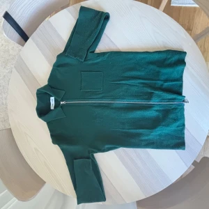 Grön Zip från samsoe samsoe - Mörkgrön kofta från Arket med hel dragkedja framtill och klassisk krage. Tröjan har lång ärm och en diskret bröstficka. Perfekt för lager-på-lager och enkel att matcha med jeans eller kjol.