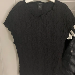Svart krinklad topp från Lindex XS - Säljer en svart krinklad topp från Lindex i storlek XS. Toppen har en crinklad struktur och korta ärmar med lätt vågig kant vid halsringningen. Perfekt för dig som gillar en enkel men ändå cool look.