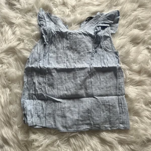 Ljusblå volangblus från SHEIN - Supersöt ljusblå blus från SHEIN med volangdetaljer vid axlarna. Ärmlös modell i tunn bomull, perfekt för varma dagar. Blusen har en lätt v-ringning och en luftig passform som ger en chill vibe till din outfit.