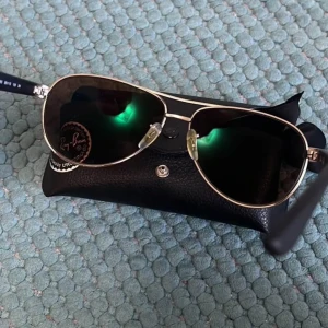 Ray-Ban solglasögon  - Ray-Ban  solglasögon med klassisk pilotform och tunna silverfärgade metallbågar. Dessa köpte jag från synoptik för många år sen (med min styrka på glasen) men har inte kommit mycket till använding. Har fått med ett par extra linser som man ser på bilden (mörkgråa) så man kan använda dom som vanliga solglasögon utan styrka. Medföljer Ray-Ban fodral och putsduk. En av dom extra glasen har en väldigt liten repa då jag råkade tappa den när jag skulle fota