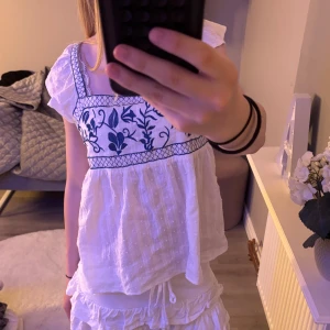 Vit blus med blå broderi - vit blus med blå broderade blommor och rutmönster upptill. 