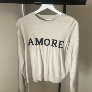 Stickad tröja ”amore” - Säljer en beige stickad tröja med svart text 'AMORE' framtill från Gina Tricot Young. Super skön och passar XS/S. Säljer då den ej kommer till användning❣️