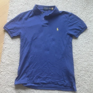 Blå Polo Ralph Lauren Piké - Snygg blå t-shirt från Polo Ralph Lauren i slim fit-modell. Den är i väldigt bra skick och knappt använd. Skick 9 av 10.