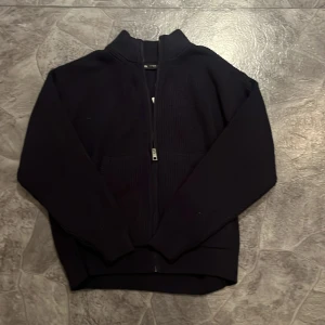 Hel zip - Säljer en stilren svart stickad kofta från Zara med dragkedja framtill. Koftan har en ribbad struktur och långa ärmar, perfekt för kyligare dagar. Enkel att matcha med olika outfits.säljer på grund av den är förstor helt ny aldrig använd lapppen sitter kvar 
