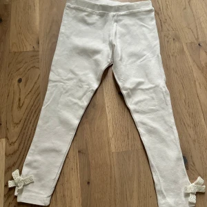 Vita leggings med spetsrosetter - Söta vita leggings från KappAhl i mjuk bomull. Smal passform med elastisk midja och fina spetsrosetter längst ner vid bensluten. Perfekta för dig som gillar en enkel men gullig stil.