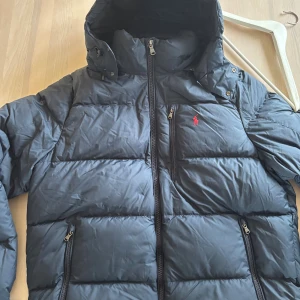 Mörkblå pufferjacka Polo Ralph Lauren  - Hej, jag säljer denna otroligt snygga och varma pufferjacka från Polo Ralph Lauren i storlek XL. Jag är använd en vinter men har ingen konstig lukt eller liknande och är exakt som den ska vara. .
