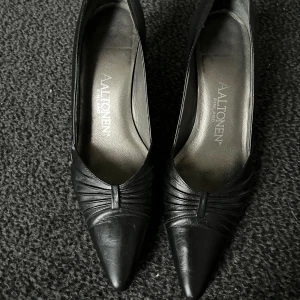 Svarta klackar från Aaltonen  - Så snygga svarta klackar från Aaltonen med spetsig tå och låg klack. Skorna är tillverkade i skinn och har snygga veckade detaljer framtill som ger en elegant look. Perfekta för dig som gillar stilrena och tidlösa skor. Vid frågor hör av dig!