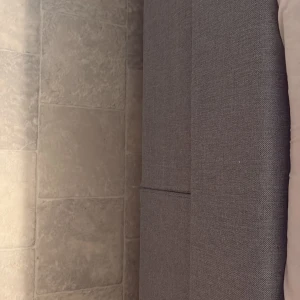 Säng - Bilderna visar en möbel, troligen en sänggavel eller soffa, klädd i grått tyg. Ingen elektronik syns på bilderna, och inga synliga märken, modeller eller tekniska specifikationer kan identifieras.