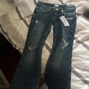 Low rise flare jeans blå Gina  - Snygga mörkblå low rise flare jeans från Ginatricot i storlek M. Jeansen har slitna detaljer, klassisk femficksmodell och kontrastsömmar. Modellen är utsvängd nertill och har låg midja för en trendig look. Perfekta för dig som gillar 00-talsvibbar.