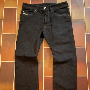 Diesel Buster svarta jeans W30 L34 - Snygga svarta Diesel Buster jeans med klassisk femficksdesign och diskreta sömmar. Jeansen är i stretchigt denim för extra komfort och har en rak passform. Perfekta för dig som gillar stilrena och tidlösa jeans med en modern touch. Uppsydda til en typ L30