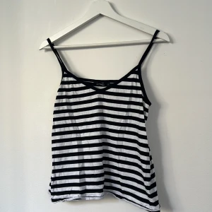 Randig linnetopp från Marimekko - Säljer en svartvit randig linnetopp från Marimekko, modell Kuulea. Toppen har smala axelband och v-ringning, perfekt för en chill och stilren look. Tillverkad i 100% bomull för en skön känsla. Passar dig som gillar klassiska mönster med en modern twist.