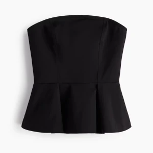 Svart peplum tubtopp - Snygg svart tubtopp med peplumskärning som ger en markerad midja och volang nertill. Toppen är axelbandslös och har en stilren, minimalistisk look. Perfekt att styla med jeans eller kjol för en trendig outfit.