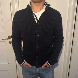 Marco Polo stickad cardigan/kofta - Säljer en mörkblå kofta med en klassisk, stilren look som passar perfekt till hösten. Skön och varm för kyligare dagar.
