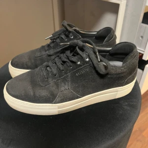 Svarta sneakers från Axel Arigato - Snygga svarta sneakers från Axel Arigato i mocka med vit platt sula. Klassisk låg modell med snörning och diskret logga på sidan. Perfekta för dig som gillar stilrena och minimalistiska skor med premiumkänsla.