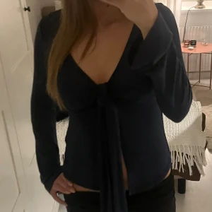 Mörkblå långärmad knytblus - Säljer en mörkblå långärmad blus med djup v-ringning och knyt framtill. 