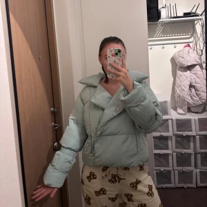 Ljusblå pufferjacka från NA-KD - Säljer en ljusblå pufferjacka från NA-KD med oversized krage och snygg asymmetrisk knäppning. Jackan är quiltad och har långa ärmar med resår vid handlederna. Perfekt för kalla dagar och riktigt trendig look.