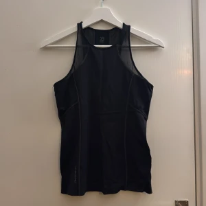 Svart träningstopp från Better Bodies - Snygg svart linnetopp från Better Bodies med meshdetaljer upptill och brottarrygg. Toppen är figurnära och har logga både fram och bak. Perfekt för dig som vill ha en sportig look på gymmet.