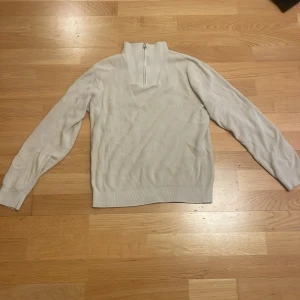 Beige stickad half zip-tröja Kappahl - Beige stickad tröja från Kappahl med ribbad struktur och half zip-dragkedja i halsen. Långärmad modell med hög krage, perfekt för lager-på-lager. Enkel och stilren design som funkar till det mesta.