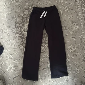 Svarta mjukisbyxor från Russedress - Svarta mjukisbyxor från Russedress med vit snörning i midjan. Byxorna har raka ben och är tillverkade i mjukt material som känns skönt mot huden. Perfekta för chill dagar eller när du vill vara extra bekväm. Och det här passar för långa personer själv är jag 168 o de är ganska långa o stora för mig