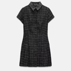 Rutig svart kortklänning från Zara - Kortärmad svart klänning från Zara med vitrutigt mönster, klassisk krage och knappar framtill. Klänningen har en figurnära passform och är sydd i ett strukturerat tyg som ger en cool och stilren look.