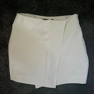Vita kjolshorts från Zara XS - Snygga vita kjolshorts från Zara i omlottmodell. Kjolen har en stilren look med rak passform och är perfekt för dig som gillar minimalistisk stil. Tillverkad i ett mjukt material som känns bekvämt mot huden. Otroligt fin tydlig vit färg!