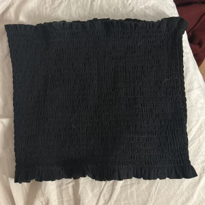 Svart bandeau tubtopp från H&M - Svart bandeau tubtopp från H&M i smockad bomull med volangkant upptill och nedtill. Toppen är ärmlös och har en tight passform som sitter snyggt på kroppen. Perfekt för varma dagar eller lager på lager. Aldrig använd men så snygg!❣️