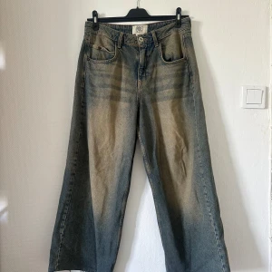 Wide jeans från BDG i tvättad blå - Säljer ett par riktigt snygga jeans från BDG med breda ben och cool tvättad blå färg. Klassisk femficksmodell, hög midja och slitna detaljer längst ner. Har en bläck fläck på höger bak ficka.