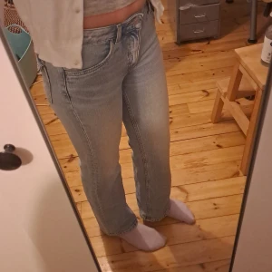 Ljusblå bootcut jeans med fickdetaljer - Säljer ett par ljusblå jeans med bootcut ben och snygga fickor med knapp bak. Jeansen har klassisk femficksdesign, normal passform och är tillverkade i mjukt denimtyg. Perfekta för en chill och stilren look.