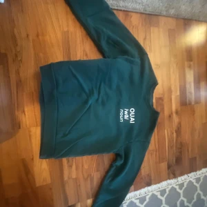 Mörkgrön sweatshirt från OUAI XL - Mörkgrön sweatshirt från OUAI i storlek XL. Tröjan har tryckt text fram och bak med definition av 'OUAI'. Mjuk insida och klassisk passform med rund hals och långa ärmar. Perfekt för chill dagar eller när du vill ha en enkel men snygg look.